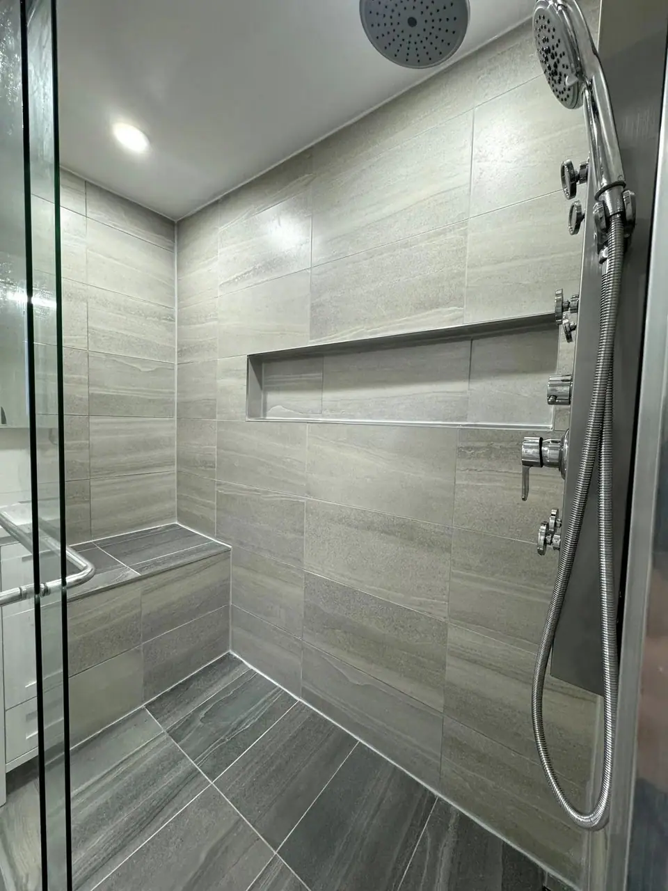A finished tiled walk-in shower with a bench, long niche and glass enclosure