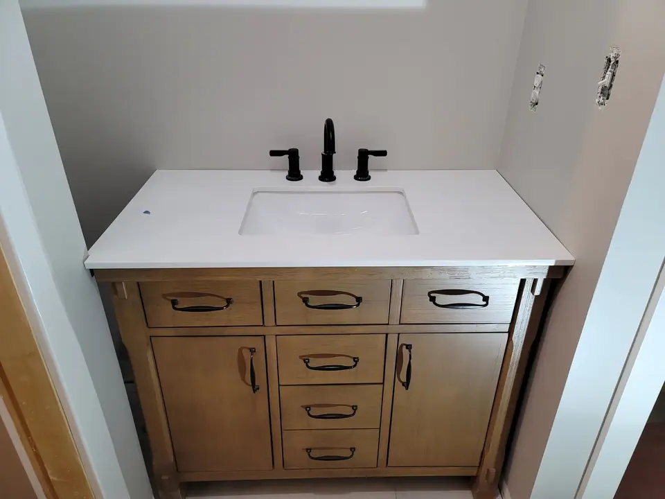 A finished wood vanity with a white top and matte black faucet, by Zenith