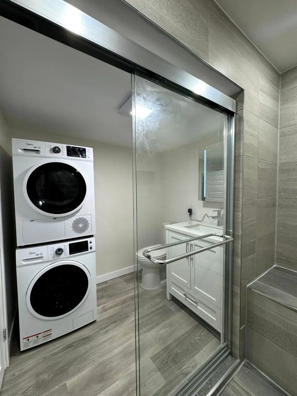 A finished compact bathroom with a glass shower and a stacked washer and dryer